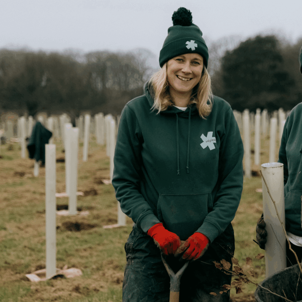 Laura Hudspith, wearing a Hiyield jumper and hat, is planting trees in a field.