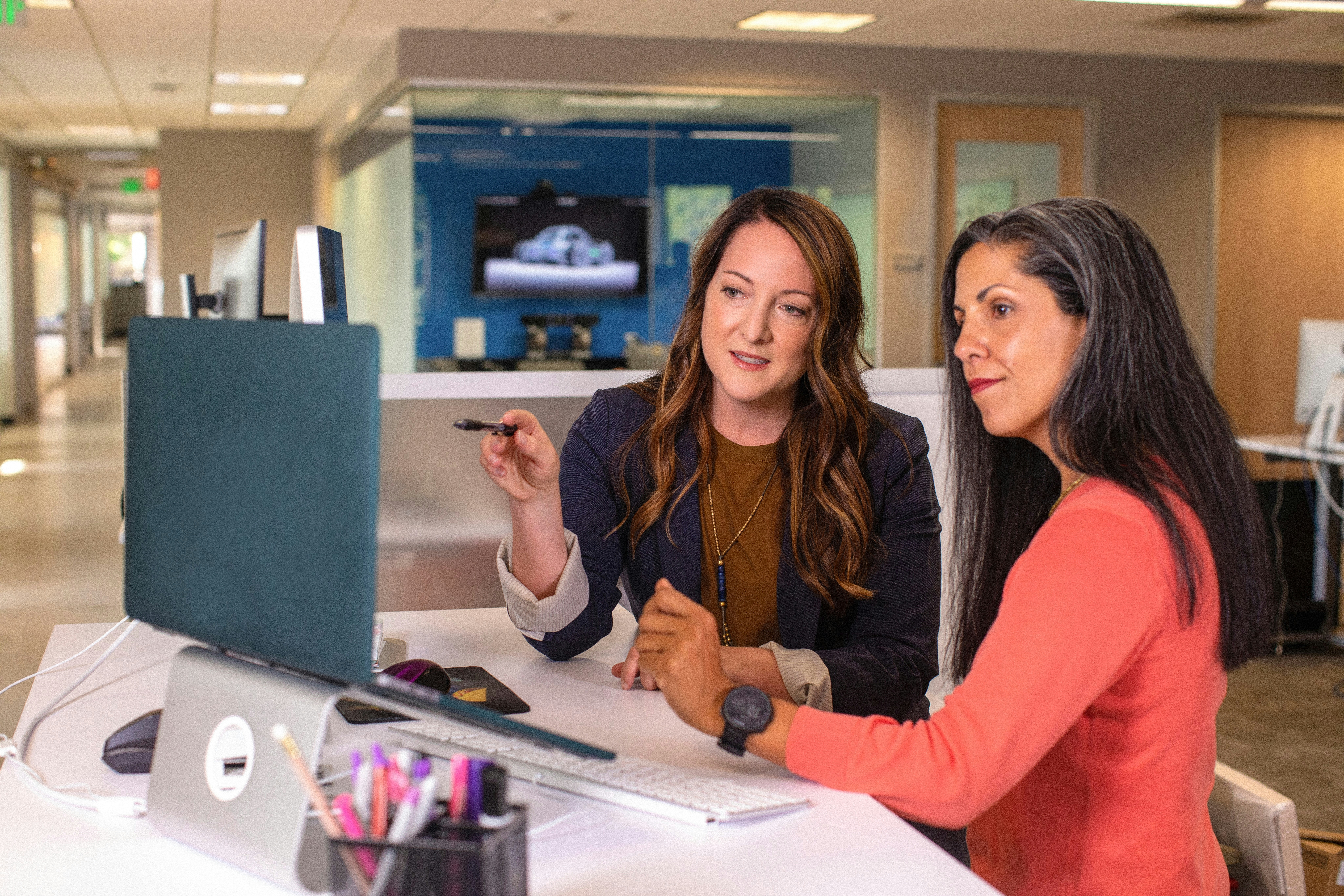 Two women are sat looking at a computer together, one woman is older with greying hair, the other is slightly younger with brown hair.