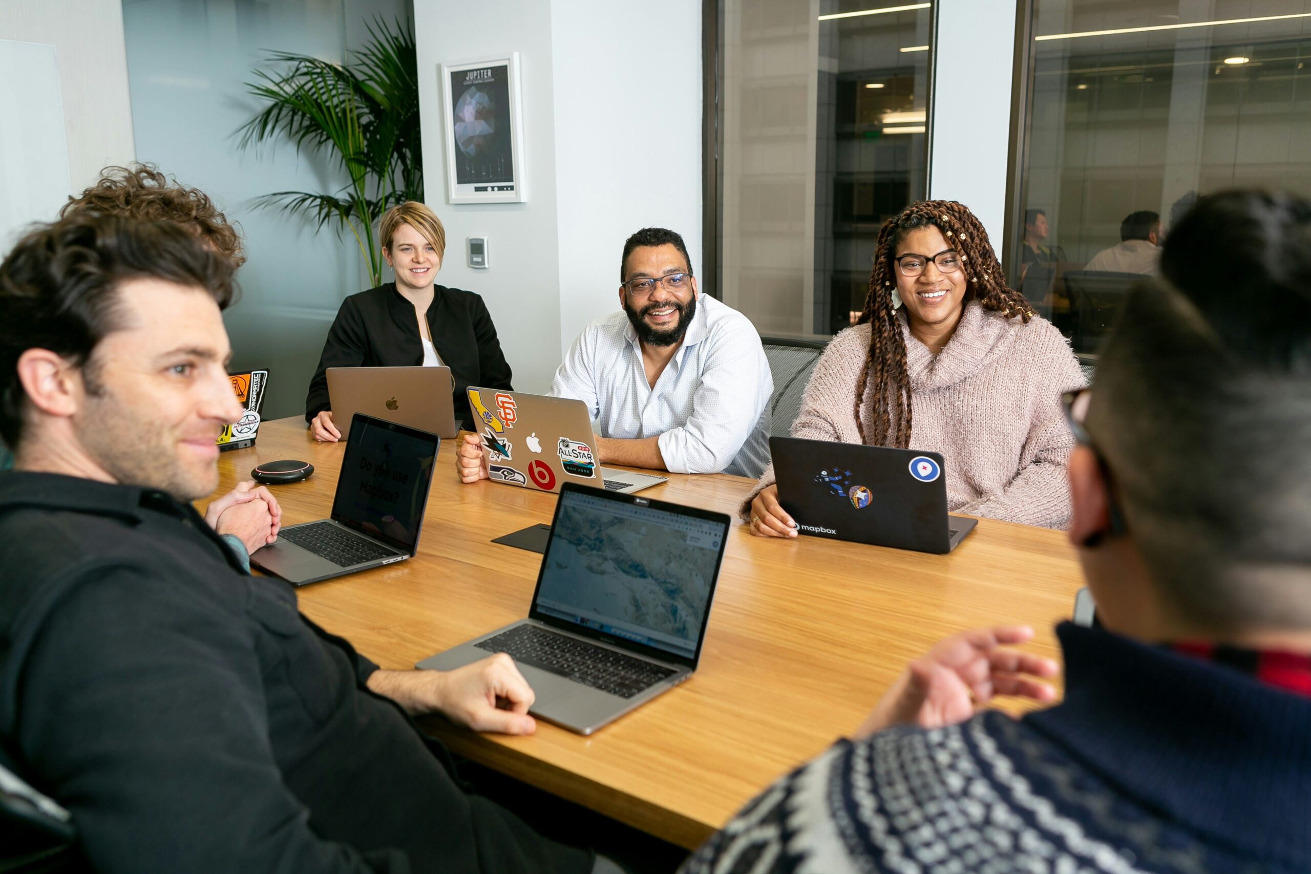 creative agency team of three men and three women sit around a table with laptops, looking at each other smiling.