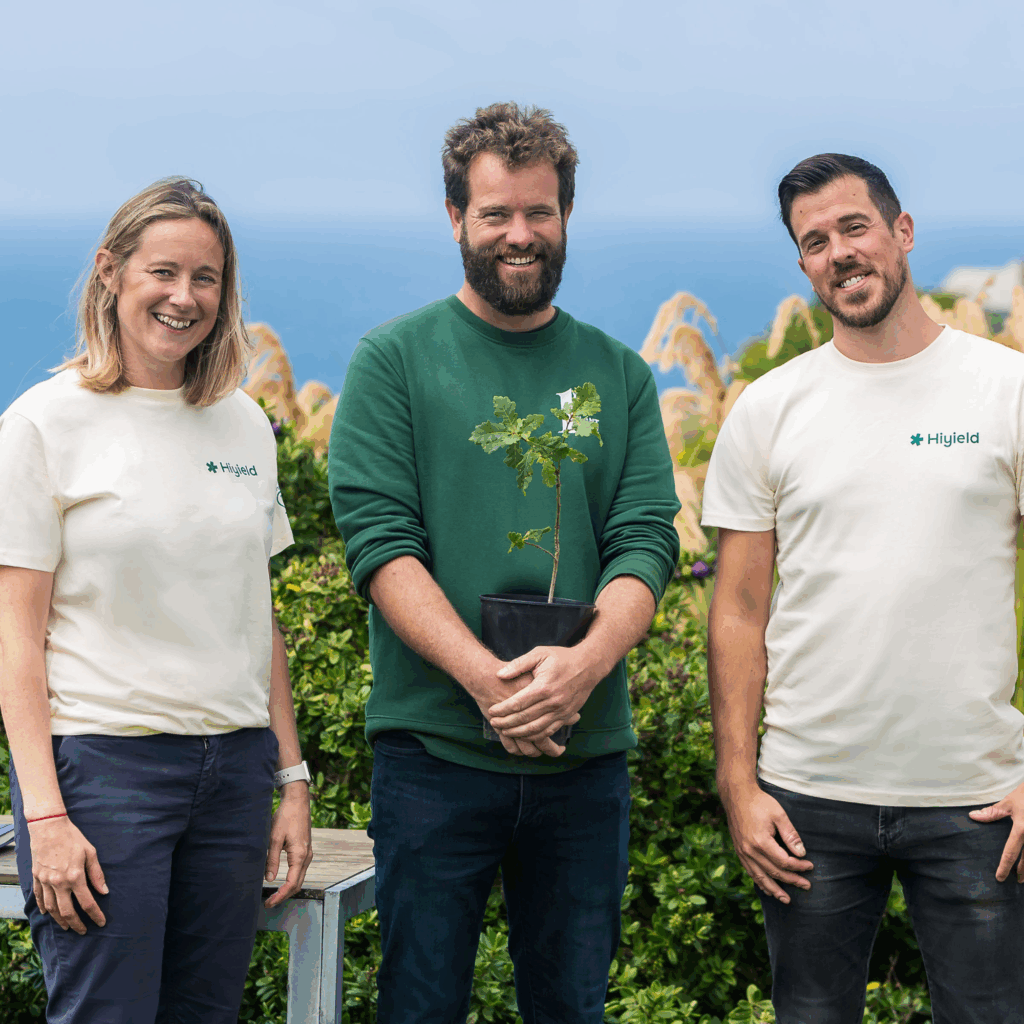 Laura Hudsptih and Matt Ville from Hiyield stood on the cliffs with the sea behind them, with them is Carl from Plant One CIC holding a tree ready for planting.
