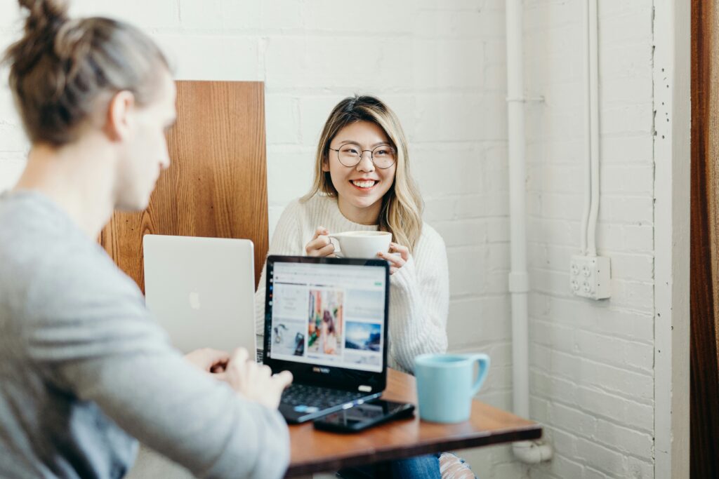 Woman drinking coffee, smiling at her colleague on a laptop.