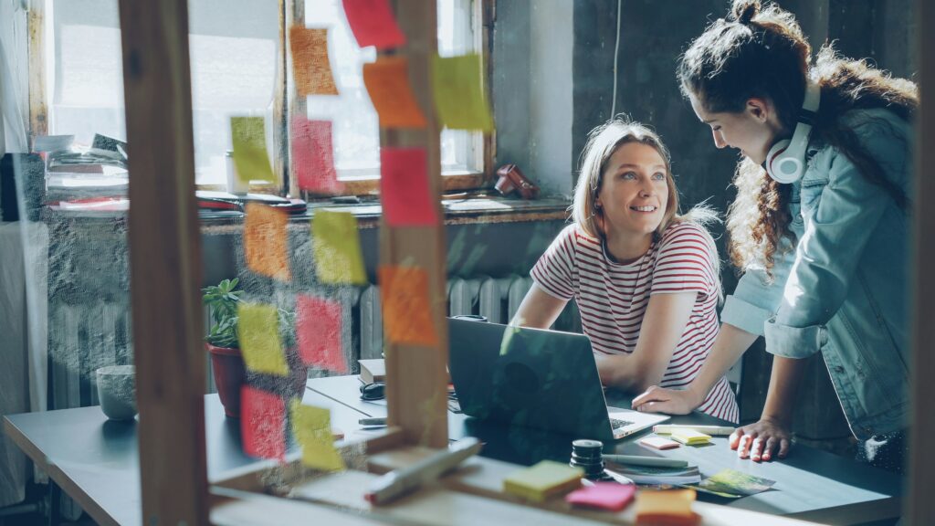 Two trendy young creative women leaning over a desk surrounded by post-its.