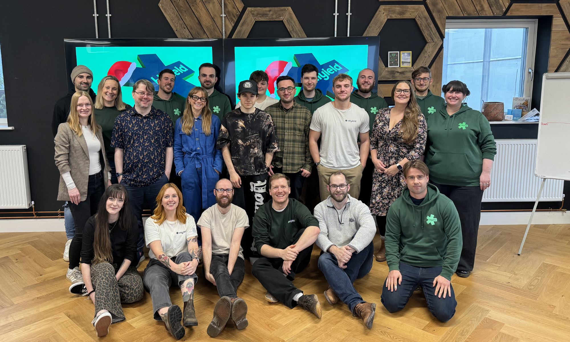 The Hiyield team posing for a group photo infront of tv screens with their logo.