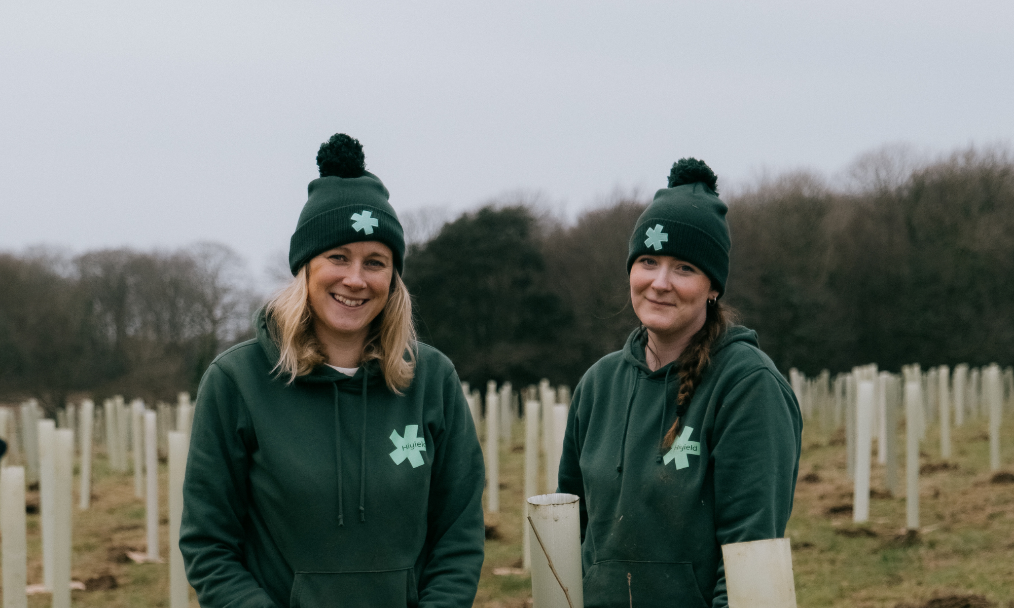 Laura and Rachel tree planting in their Hiyield hats and hoodies.