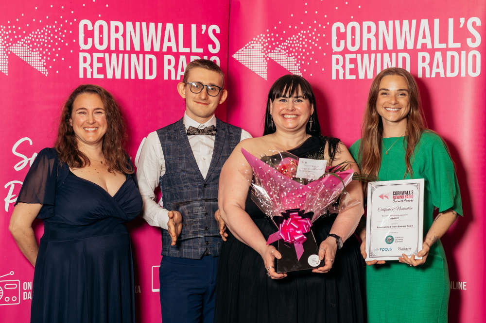 Justin, Lyssa, and Sophie holding their award and flowers infront of the Cornwall's Rewind Radio step and repeat - with the judge who gave them the award. 