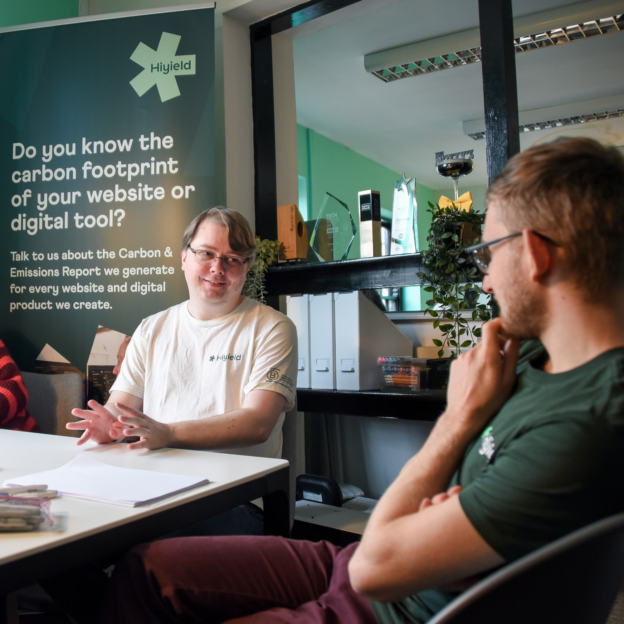 Hiyield team Ben and Justin sat at a table with banner behind talking about climate conscious software development.